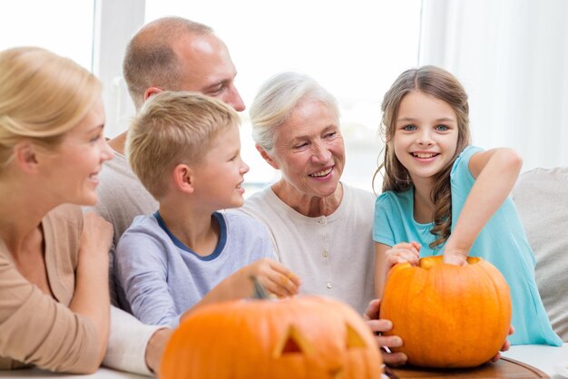 concetto di famiglia, felicità, generazione, vacanze e persone - famiglia felice che fa zucche di Halloween a casa