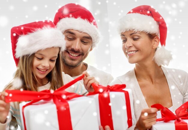 concetto di famiglia, felicità, generazione, vacanze e persone - famiglia felice in cappelli di Babbo Natale con scatole regalo seduti sul divano a casa