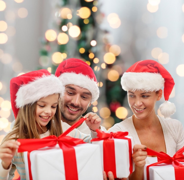 concetto di famiglia, felicità, generazione, vacanze e persone - famiglia felice in cappelli di Babbo Natale con scatole regalo su sfondo di luci dell'albero di Natale