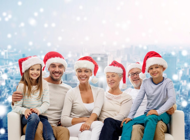 concetto di famiglia, felicità, generazione, vacanze e persone - famiglia felice in cappelli di Babbo Natale seduto sul divano su sfondo di città innevata