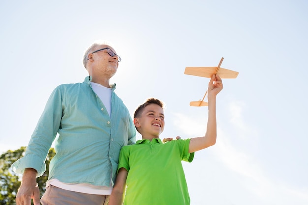 concetto di famiglia, generazione, futuro, sogno e persone - nonno e nipote felici con aeroplano giocattolo sopra il cielo blu