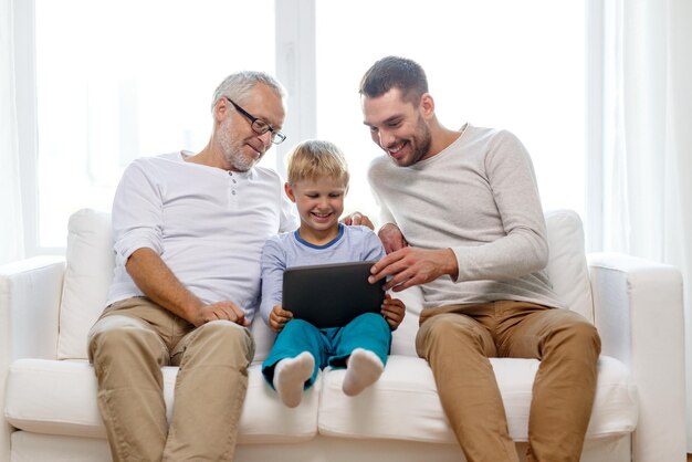 concetto di famiglia, generazione, tecnologia e persone - padre, figlio e nonno sorridenti seduti sul divano con computer tablet pc a casa