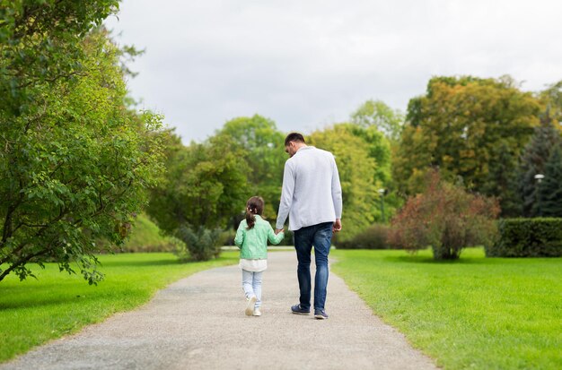 concetto di famiglia, genitorialità, paternità, adozione e persone - padre felice e bambina che camminano nel parco estivo