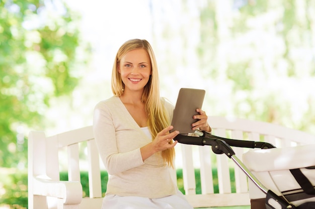 concetto di famiglia, genitorialità, tecnologia e persone - madre felice con computer tablet pc e passeggino nel parco