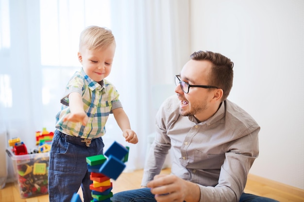 concetto di famiglia, infanzia, creatività, attività e persone - padre felice e figlio piccolo che giocano con i blocchi giocattolo a casa