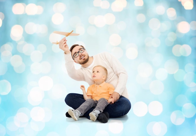 concetto di famiglia, infanzia, paternità, tempo libero e persone - padre felice e figlio piccolo che giocano con l'aeroplano giocattolo su sfondo blu luci vacanze