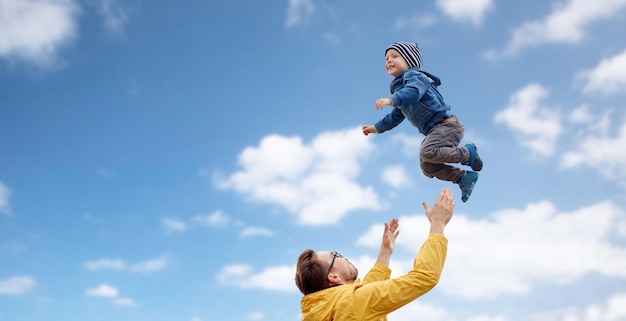 concetto di famiglia, infanzia, paternità, tempo libero e persone - padre felice e figlio piccolo che giocano e si divertono all'aperto su sfondo blu cielo e nuvole