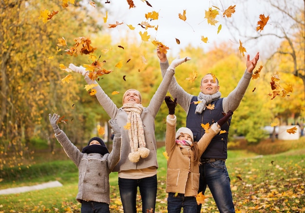 concetto di famiglia, infanzia, stagione e persone - famiglia felice che gioca con le foglie di autunno nel parco