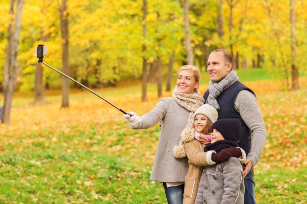 concetto di famiglia, infanzia, stagione, tecnologia e persone - famiglia felice che si fa selfie con smartphone e monopiede nel parco autunnale