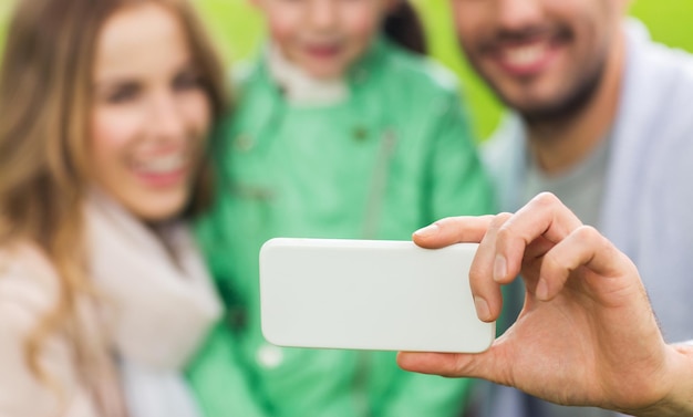 concetto di famiglia, infanzia, tecnologia e persone - primo piano di padre felice, madre e figlia piccola che prendono selfie con lo smartphone nel parco