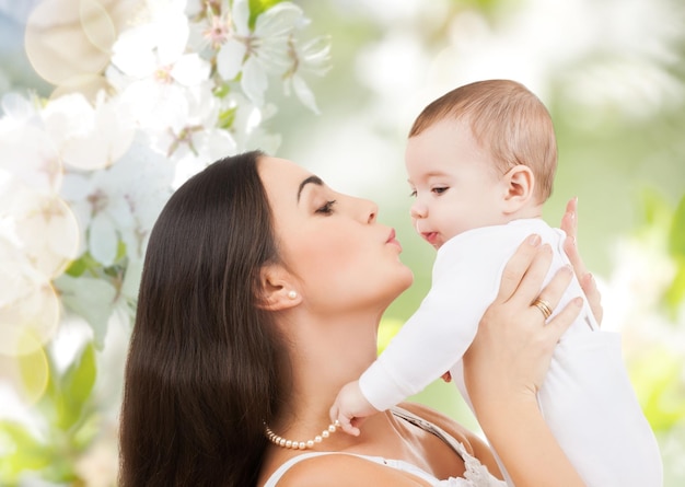 concetto di famiglia, maternità, primavera, estate e persone - bambino che ride felice che gioca con la madre su sfondo verde giardino fiorito