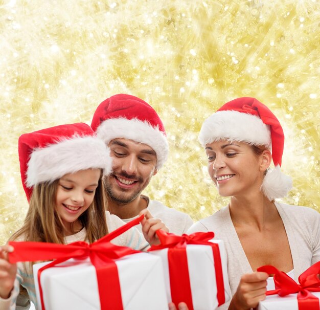 concetto di famiglia, natale, generazione, vacanze e persone - famiglia felice in cappelli di Babbo Natale con scatole regalo seduto su sfondo di luci gialle