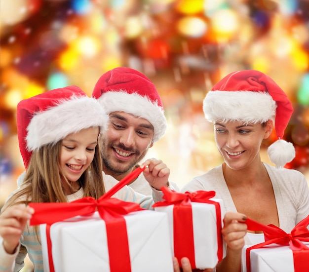 concetto di famiglia, natale, generazione, vacanze e persone - famiglia felice in cappelli di Babbo Natale con scatole regalo su sfondo a luci rosse