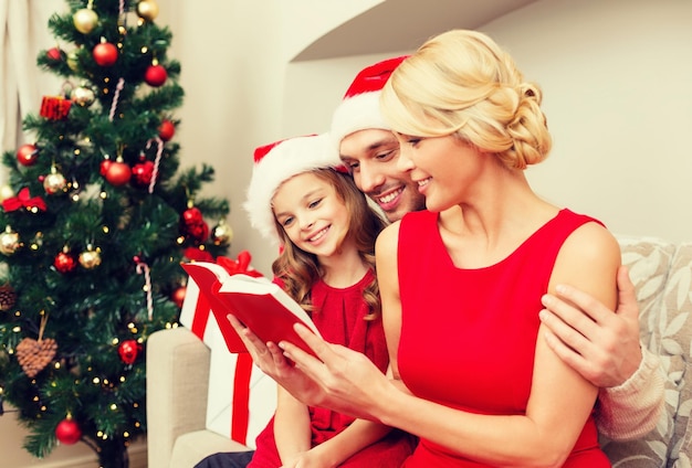 concetto di famiglia, natale, natale, felicità e persone - famiglia sorridente in cappelli di Babbo Natale con molte scatole regalo libro di lettura