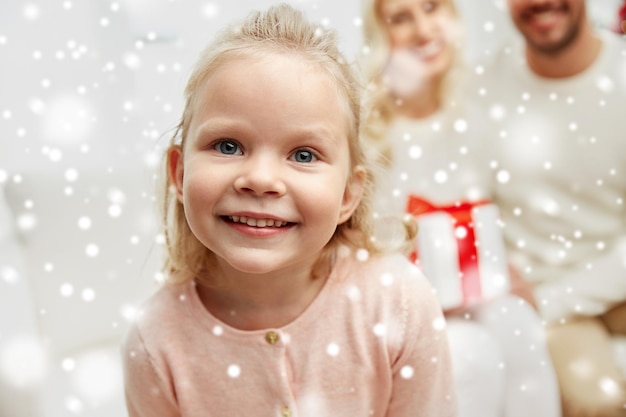 concetto di famiglia, natale, vacanze e persone - madre felice, padre e figlia piccola con confezione regalo seduta sul divano di casa