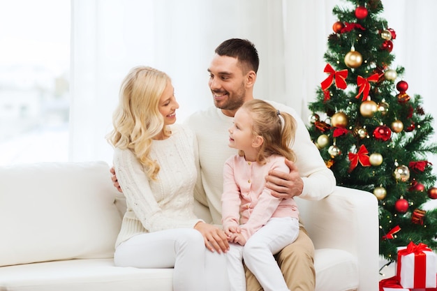 concetto di famiglia, natale, vacanze e persone - madre felice, padre e figlia piccola seduti sul divano a casa