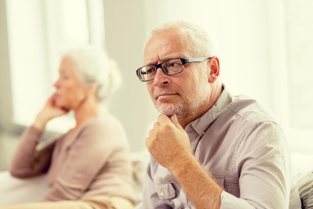 concetto di famiglia, relazioni, età e persone - coppia senior seduta sul divano a casa