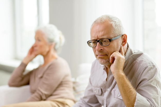 concetto di famiglia, relazioni, età e persone - coppia senior seduta sul divano a casa