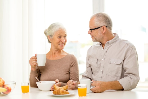 concetto di famiglia, tecnologia, cibo, bevande e persone - coppia senior felice che fa colazione a casa