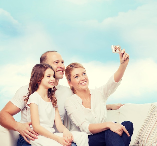 concetto di famiglia, tecnologia e persone - madre, padre e bambina sorridenti che fanno selfie con la fotocamera su sfondo blu cielo