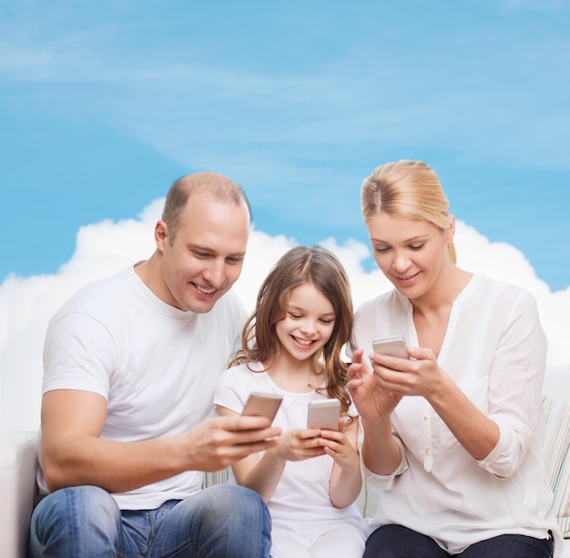 concetto di famiglia, tecnologia e persone - madre, padre e bambina sorridenti con smartphone su sfondo blu cielo e nuvola bianca