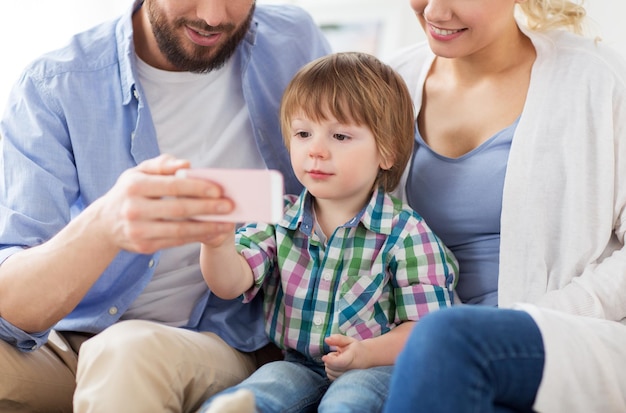 concetto di famiglia, tecnologia e persone: madre, padre e ragazzino felici con lo smartphone a casa