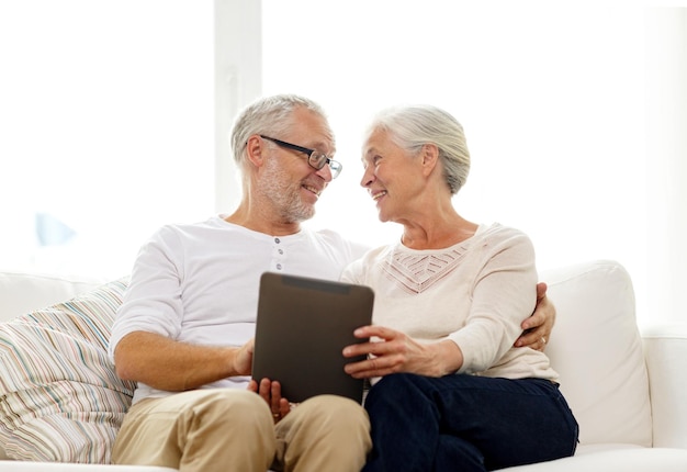 concetto di famiglia, tecnologia, età e persone - coppia senior felice con computer tablet pc a casa