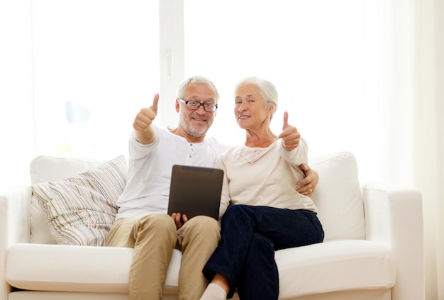 concetto di famiglia, tecnologia, età, gesto e persone - coppia senior felice con computer tablet pc che mostra i pollici in su a casa