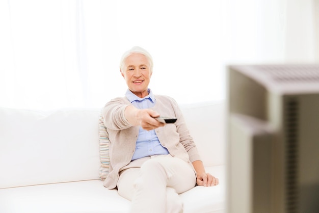 concetto di famiglia, tecnologia, televisione, età e persone - donna anziana felice che guarda la tv a casa