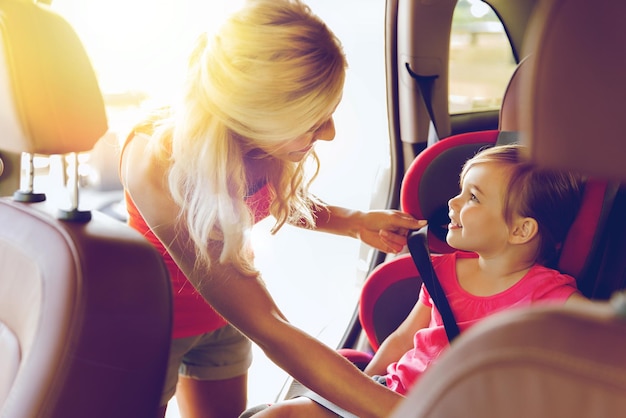 concetto di famiglia, trasporti, sicurezza, viaggio su strada e persone - madre felice che fissa il bambino con la cintura di sicurezza dell'auto