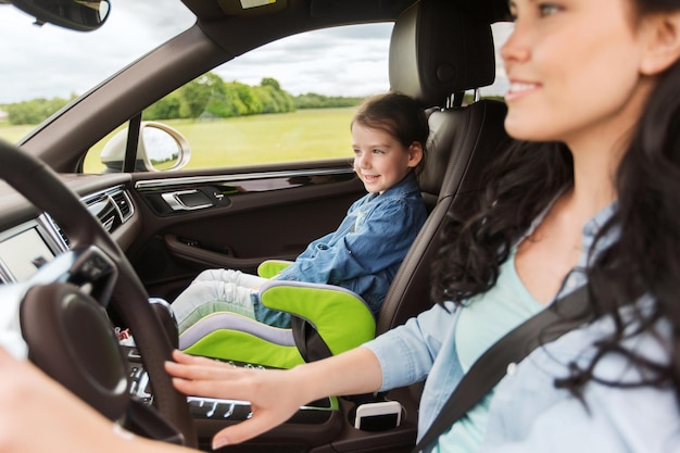 concetto di famiglia, trasporto, viaggio su strada e persone - donna felice con figlia piccola che guida in macchina