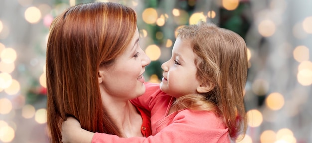 concetto di famiglia, vacanze, bambini e persone - madre felice e piccola figlia che si abbracciano sopra lo sfondo delle luci dell'albero di Natale