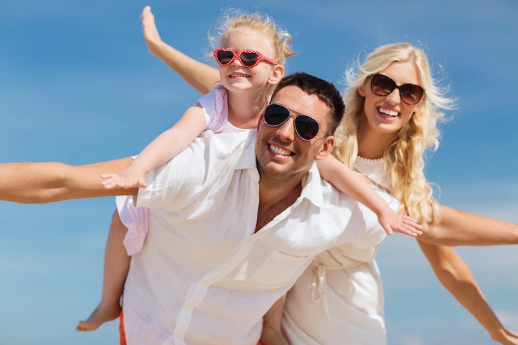 Foto concetto di famiglia, vacanze estive, adozione e persone - uomo felice, donna e bambina in occhiali da sole divertendosi su sfondo blu cielo