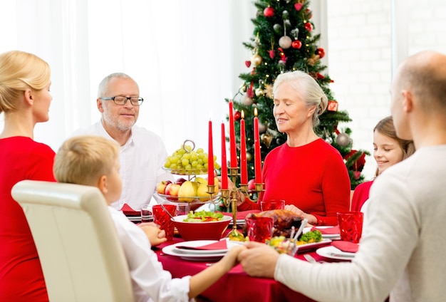 concetto di famiglia, vacanze, generazione, natale e persone - famiglia sorridente che cena e prega a casa