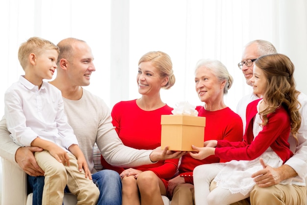 concetto di famiglia, vacanze, generazione, natale e persone - famiglia sorridente con confezione regalo seduta sul divano a casa