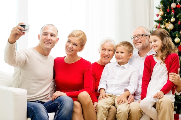 concetto di famiglia, vacanze, generazione, natale e persone - famiglia sorridente con fotocamera che fa selfie e seduto sul divano a casa