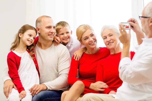 concetto di famiglia, vacanze, generazione, natale e persone - famiglia sorridente con fotocamera che fotografa e si siede sul divano a casa