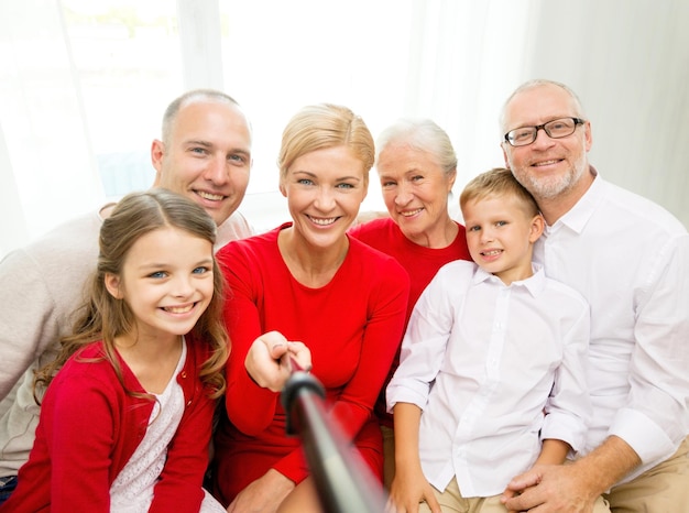 concetto di famiglia, vacanze, generazione, natale e persone - famiglia sorridente con fotocamera e selfie stick che fa foto a casa