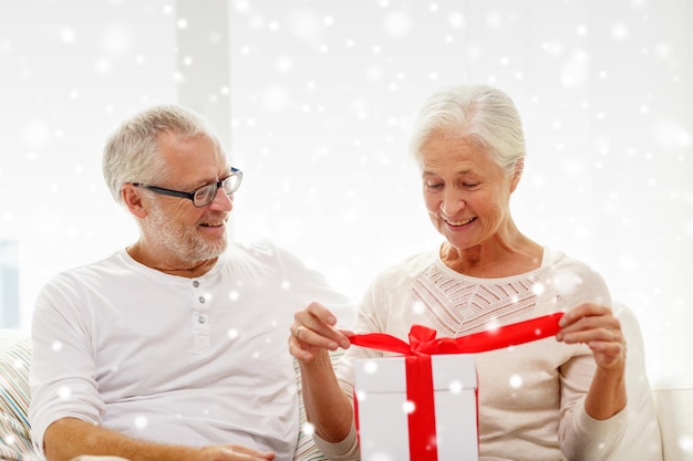 concetto di famiglia, vacanze, natale, età e persone - coppia senior felice con confezione regalo a casa