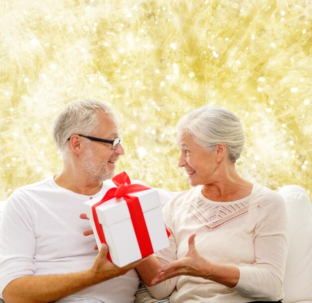 concetto di famiglia, vacanze, natale, età e persone - coppia senior felice con confezione regalo su sfondo a luci gialle