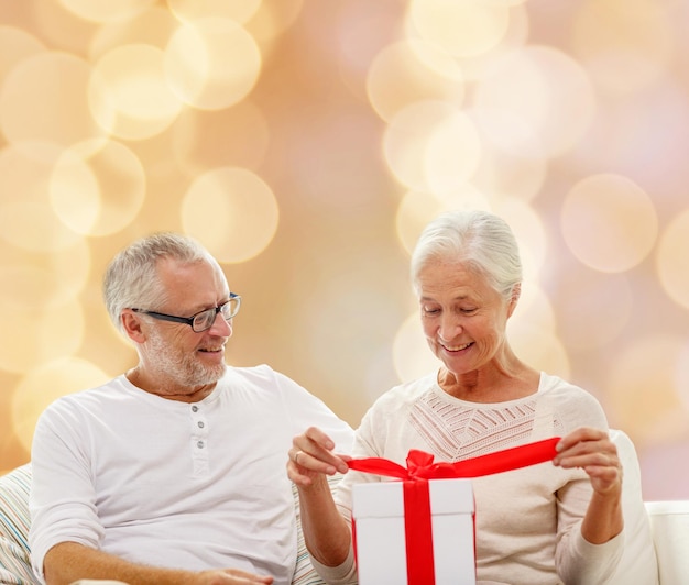 concetto di famiglia, vacanze, natale, età e persone - coppia senior felice con confezione regalo su sfondo di luci beige