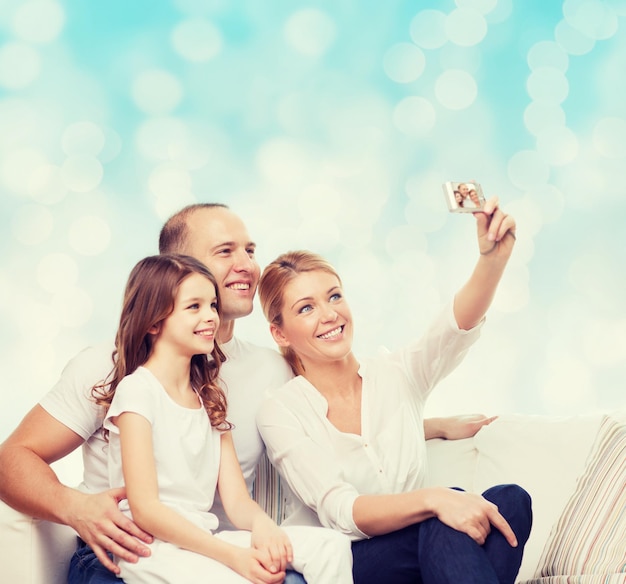 concetto di famiglia, vacanze, tecnologia e persone - madre, padre e bambina sorridenti che fanno selfie con la fotocamera su sfondo di luci blu