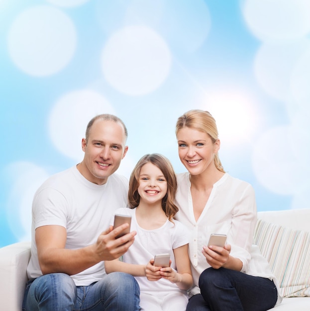 concetto di famiglia, vacanze, tecnologia e persone - madre, padre e bambina sorridenti con smartphone su sfondo di luci blu