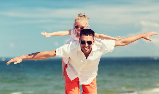 concetto di famiglia, viaggi, vacanze, adozione e persone - padre felice con una bambina in occhiali da sole che si diverte sulla spiaggia estiva