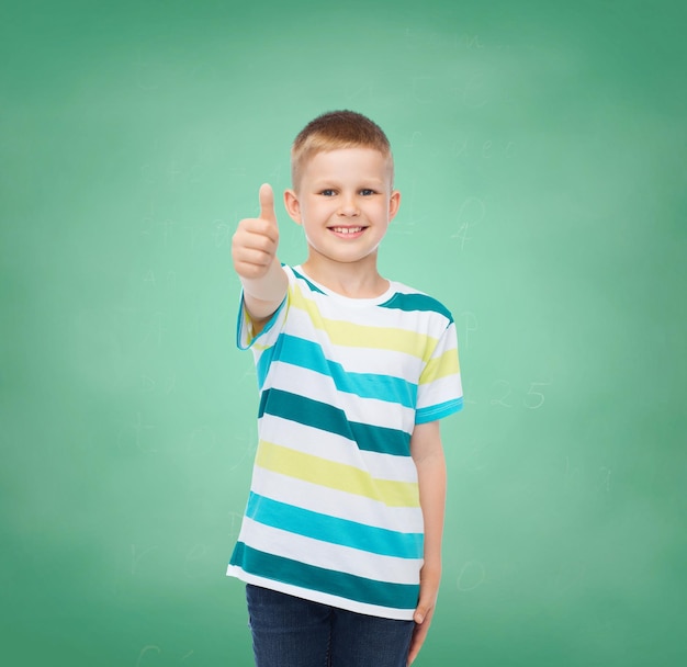 concetto di felicità, infanzia, scuola, istruzione e persone - ragazzino sorridente che mostra i pollici in su su sfondo verde