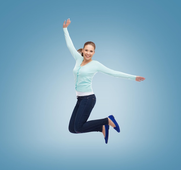 concetto di felicità, libertà, movimento e persone - giovane donna sorridente che salta in aria su sfondo blu
