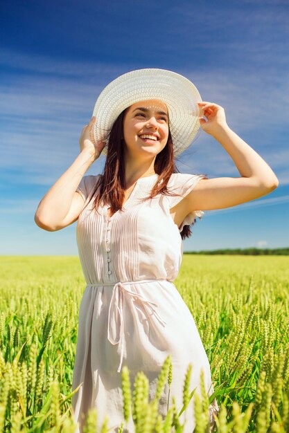 concetto di felicità, natura, estate, vacanze e persone - giovane donna sorridente che indossa il cappello di paglia sul campo di cereali