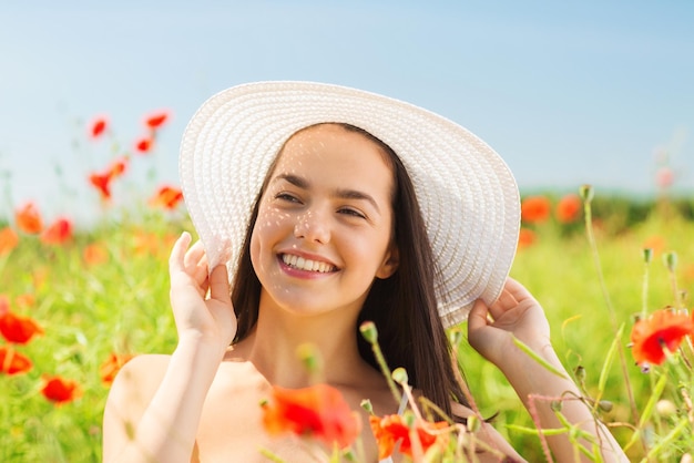 concetto di felicità, natura, estate, vacanze e persone - giovane donna sorridente che indossa il cappello di paglia sul campo di papaveri