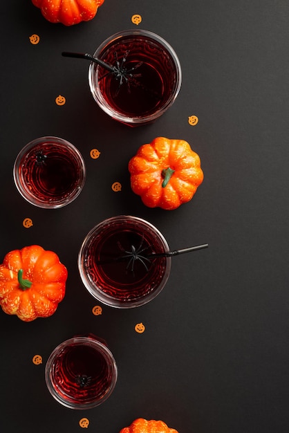 Concetto di festa di Halloween Vista dall'alto foto verticale di drink in bicchieri con ragni galleggianti cannucce zucche e confetti su sfondo nero isolato