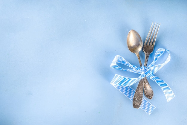 Concetto di festa di ottobre. Sfondo della tavola dell'Oktoberfest, cucchiaio forchetta piatto con tovagliolo tradizionale, servito all'evento, menu bar flatlay, tavolo blu colorato spazio copia vista dall'alto